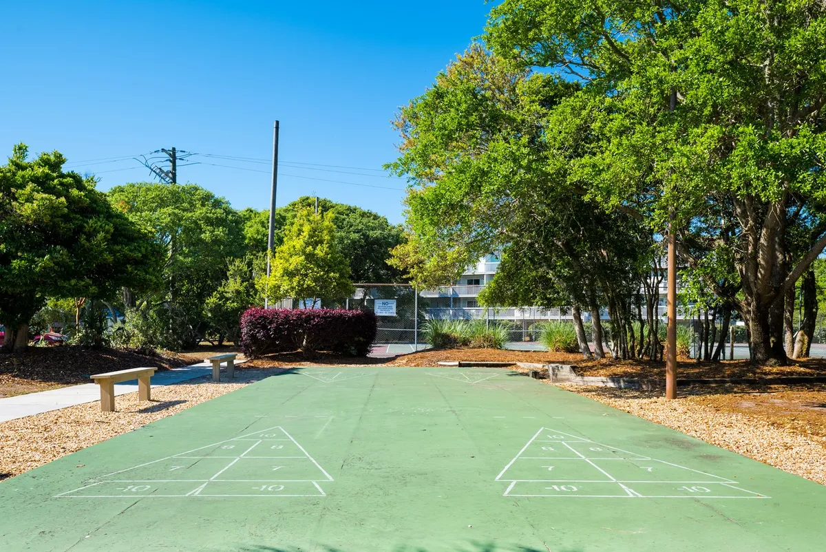 A well-maintained shuffleboard court set amidst greenery with benches for spectators or players to relax. The open outdoor area encourages playful competition and community gatherings.