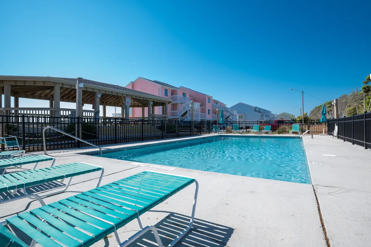 A lively pool area surrounded by lounge chairs and vibrant, colorful buildings. The pool is the centerpiece, with families or groups able to sunbathe, swim, or socialize in this welcoming outdoor space.