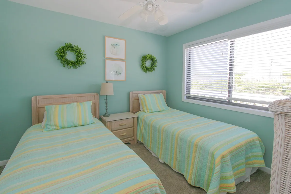 This photo displays a bedroom with twin beds, bright sunlight streaming through the window, and green wreaths above the beds. The room feels calm and refreshing, ideal for guests seeking relaxation or quiet moments.