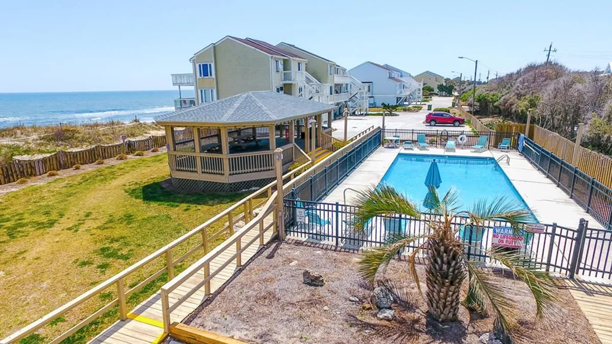 An inviting outdoor swimming pool framed by a gazebo, palm trees, and an ocean view in the background. The pool area features lounge chairs for sunbathing and spaces for social gatherings or quiet relaxation.