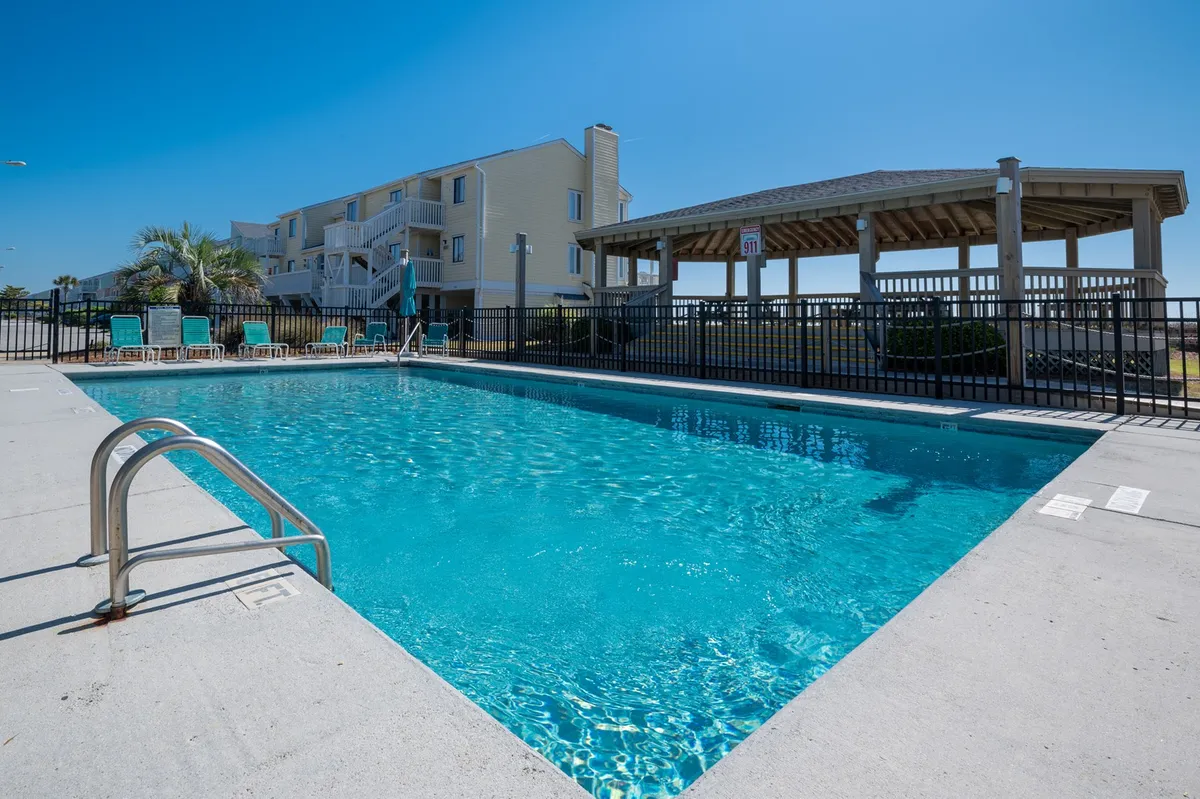 A large swimming pool surrounded by lounge chairs and a gazebo, framed by lush greenery. The area invites socializing, swimming, and relaxation, emphasizing communal resort-style amenities. The open space is ideal for group fun and unwinding after exploring local attractions.