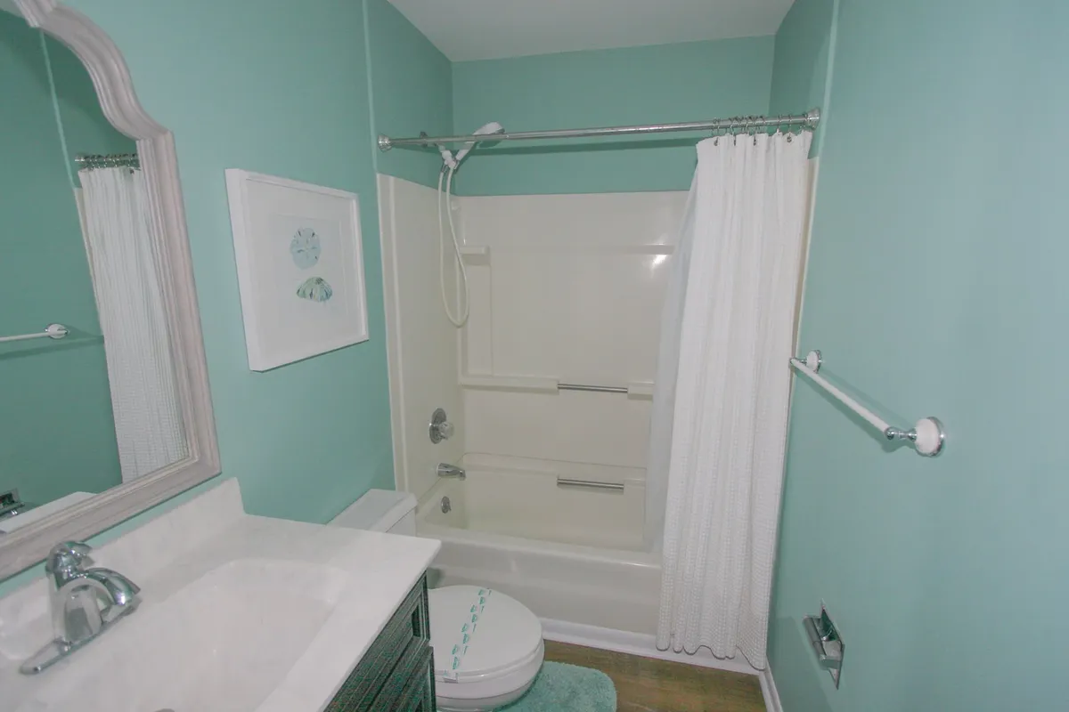 This interior bathroom features mint green walls, a crisp white shower curtain, and a modern sink, all contributing to a fresh and serene ambiance. The space is clean, inviting, and practically designed for relaxation and comfort.