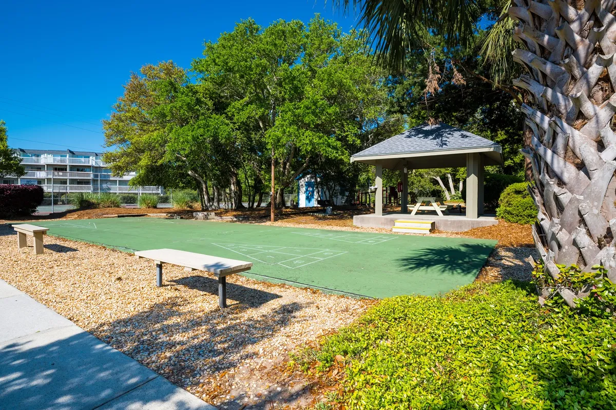 This image shows a vibrant green court with a gazebo, surrounded by trees and benches, suggesting a space for play, picnics, or quiet reflection in a natural setting.