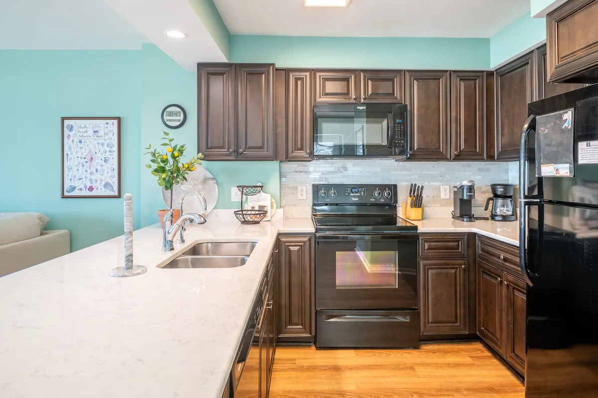 A modern laundry area is integrated with the kitchen, featuring dark wood cabinetry, a white marble countertop, and stainless steel appliances. The space is tidy and practical, with a decorative vase adding a homely touch.