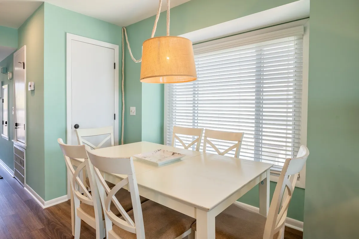 A cozy dining area with a wooden table set under a hanging lamp, next to a window with soft natural light. The space is set for family meals, games, or special occasions, promoting a sense of closeness and comfort.